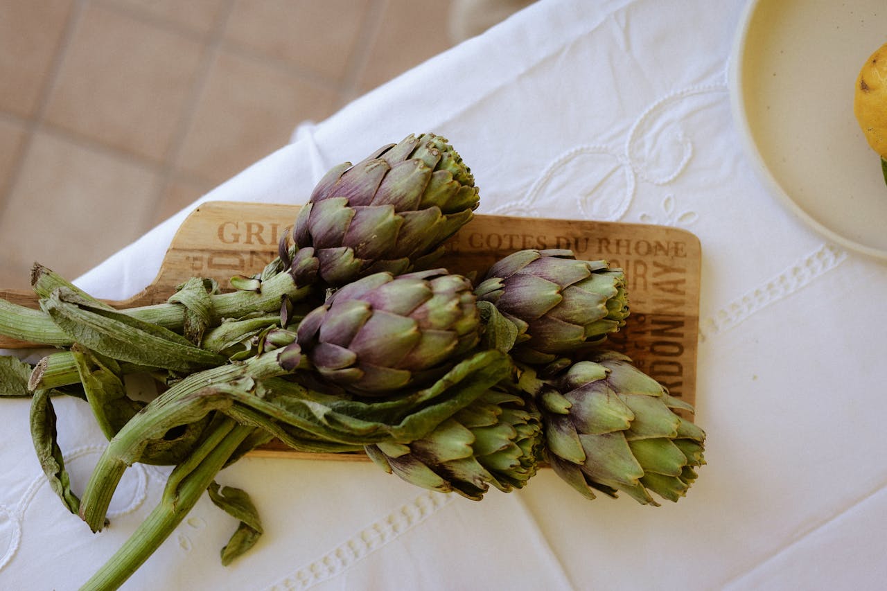 A bunch of fresh artichokes displayed on a wooden board, evoking a rustic kitchen setting.