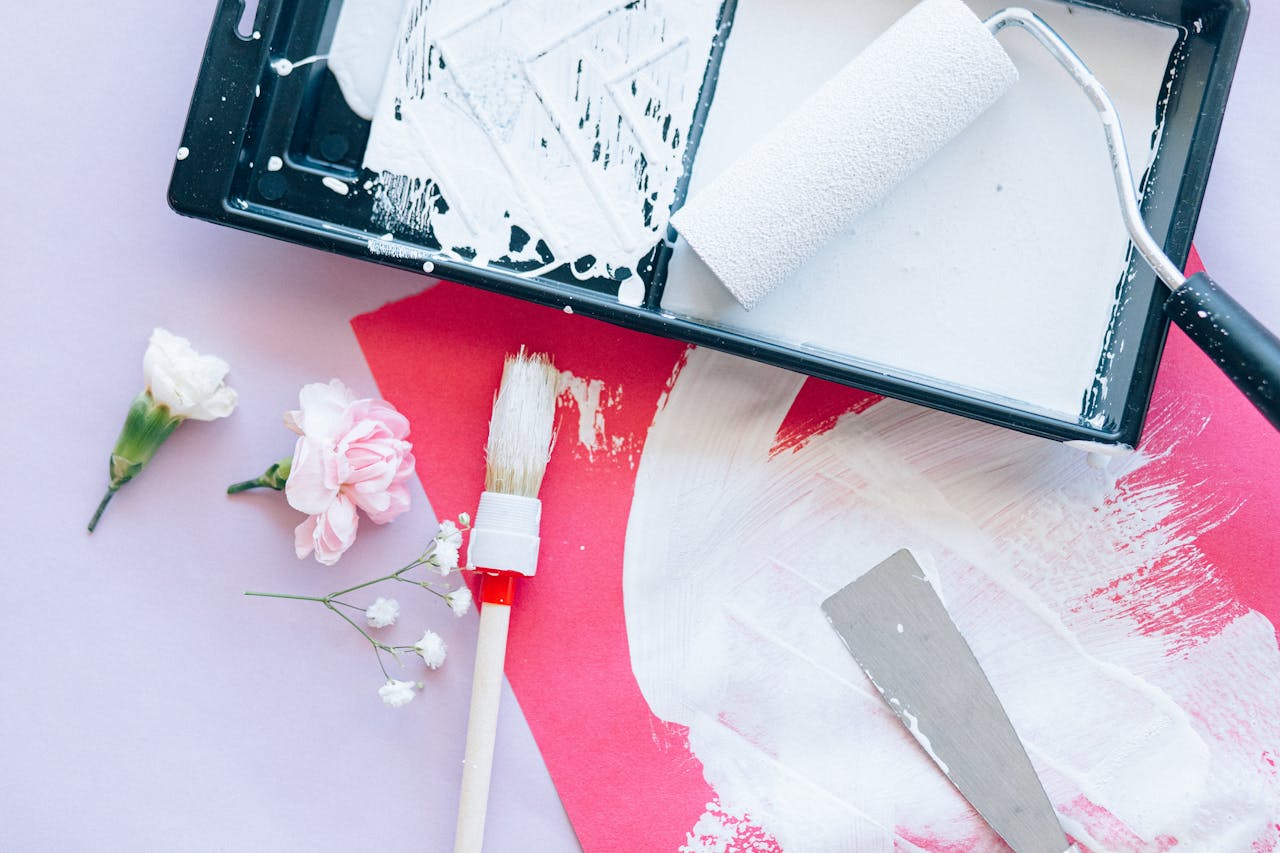 Artistic arrangement of flowers with a paint roller and tools on a pink painted surface.