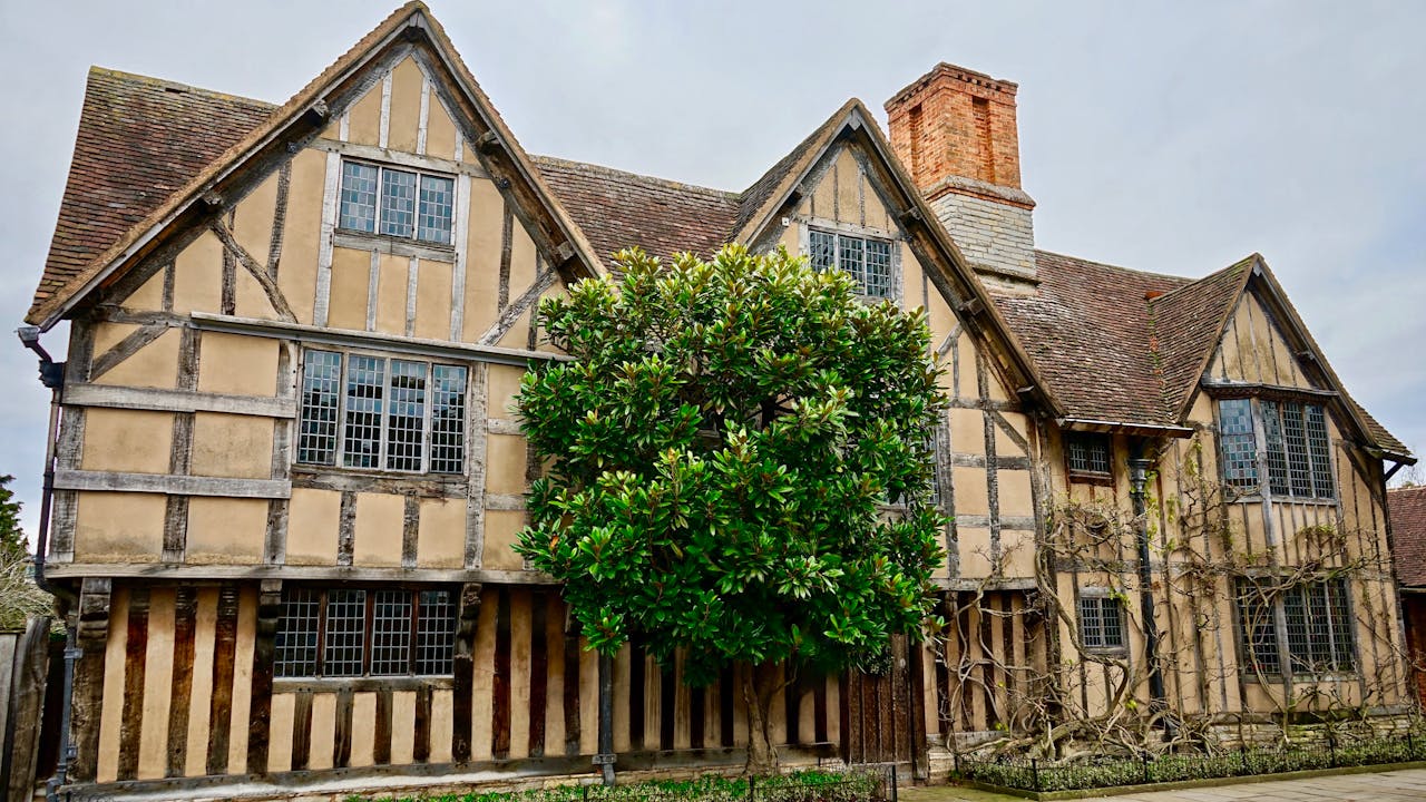 A beautifully preserved Tudor-style house with detailed woodwork and lush greenery, captured in daylight.